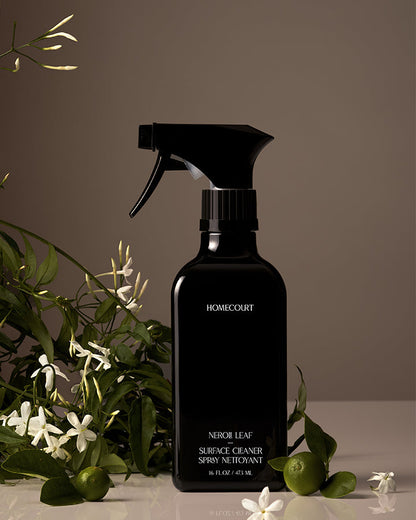 Black spray bottle labeled 'Homecourt' with green leaves and white flowers in the background