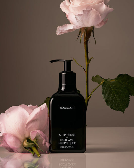 Black pump bottle of Homecourt Steeped Rose Hand Wash with pink roses on a neutral background