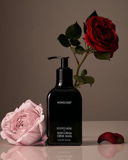 Black hand cream bottle labeled 'Homecourt' with pink and red roses on a reflective surface.