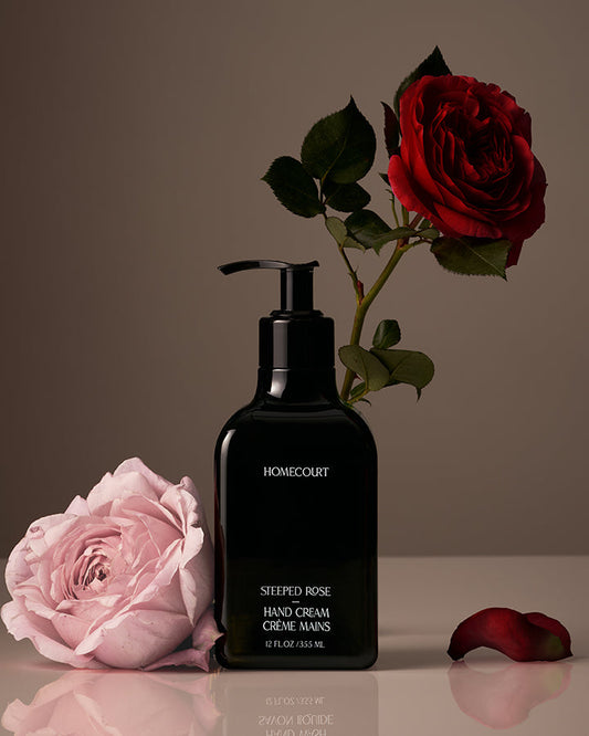 Black hand cream bottle labeled 'Homecourt' with pink and red roses on a reflective surface.