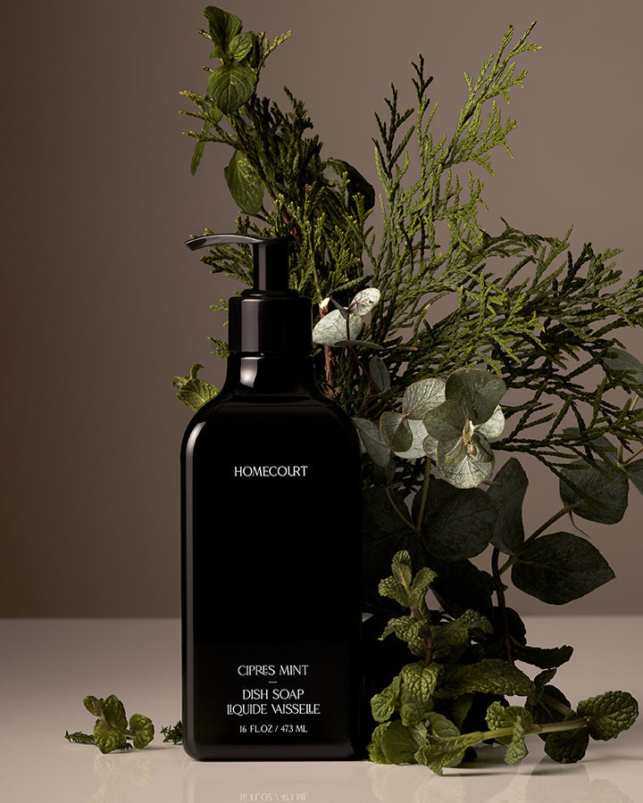 Black soap dispenser with 'Homecourt' branding surrounded by greenery on a neutral background