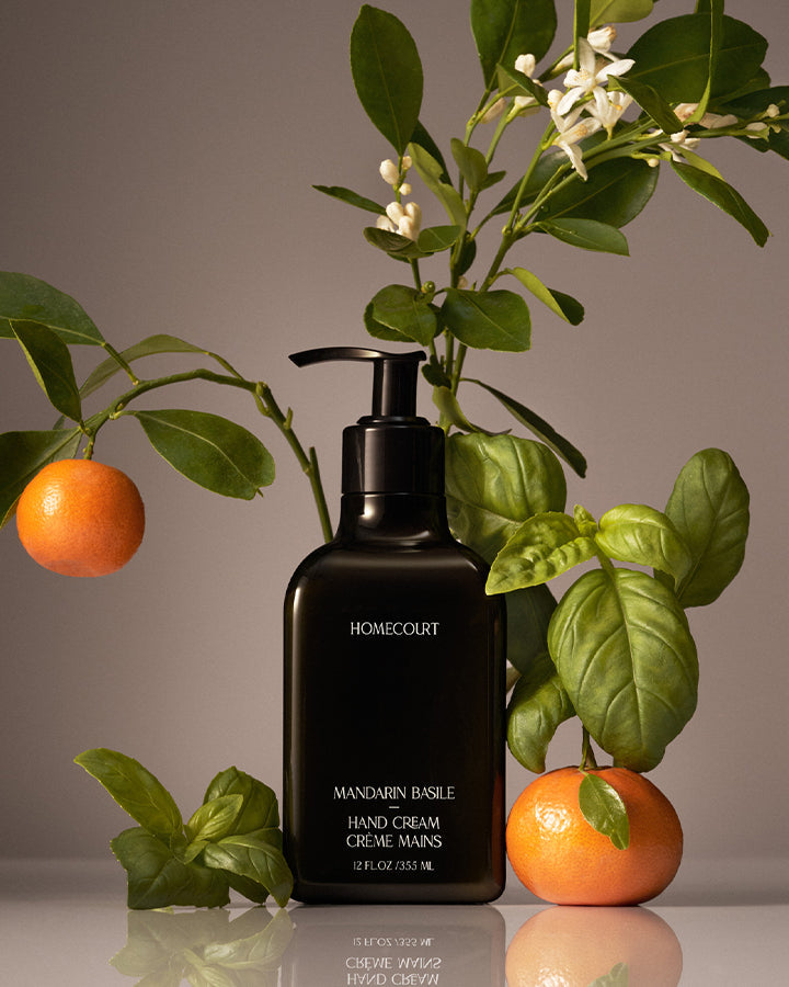 Black hand cream bottle labeled 'Homecourt' with mandarin oranges and leaves on a reflective surface.