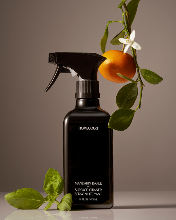 Black spray bottle labeled 'Homecourt' with mandarin orange and leaves on a neutral background