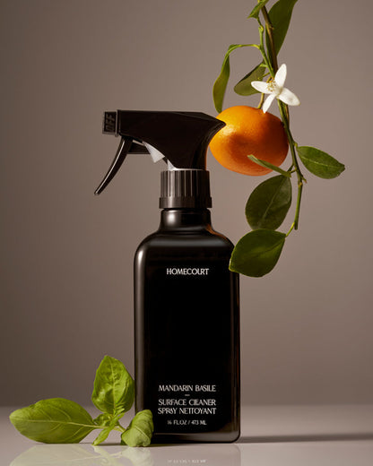 Black spray bottle labeled 'Homecourt' with mandarin orange and leaves on a neutral background