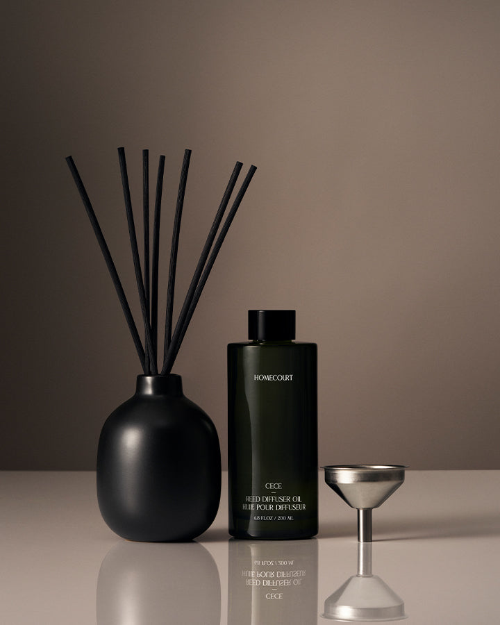 Black diffuser bottle with reeds and a small container on a reflective surface with a brown background