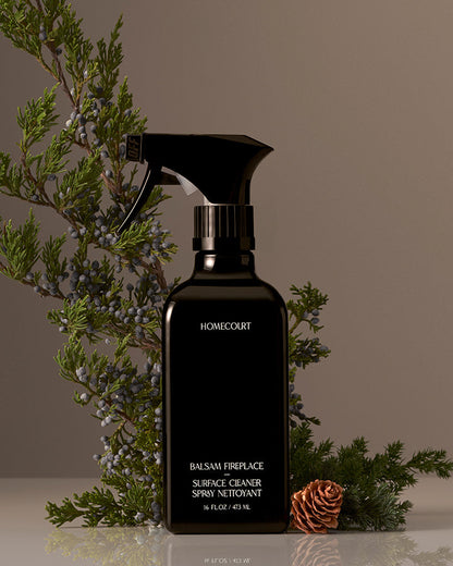 Black spray bottle labeled 'Homecourt' with decorative evergreen branches on a neutral background