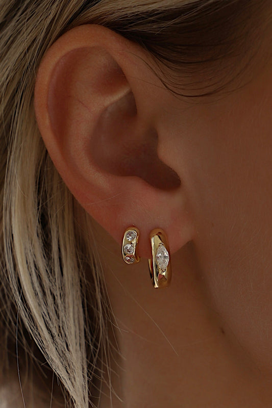 Gold earrings worn on an ear with a blurred background