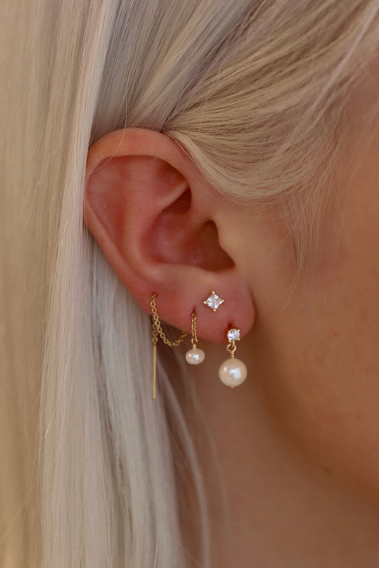 Close-up of an ear wearing gold and pearl earrings with a neutral background