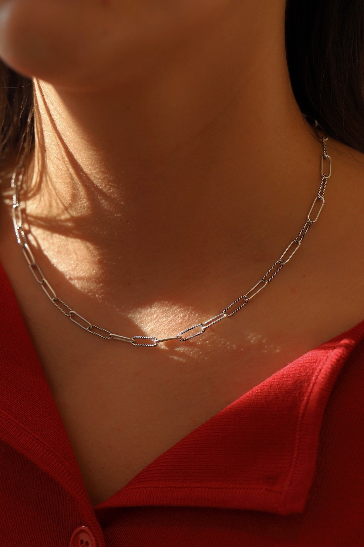 Close-up of a silver chain necklace on a person wearing a red garment.