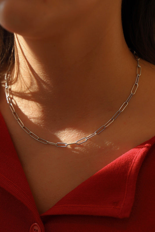 Close-up of a silver chain necklace on a person wearing a red garment.