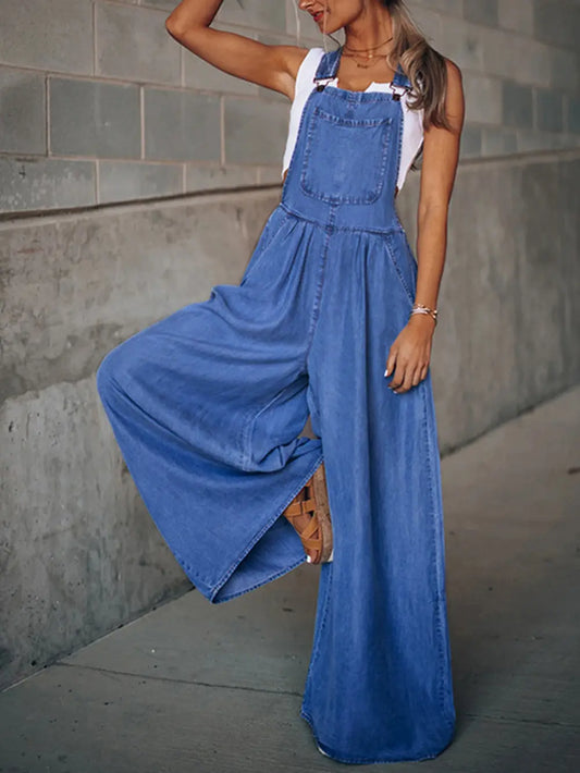 Woman wearing blue wide leg overalls posing against concrete wall