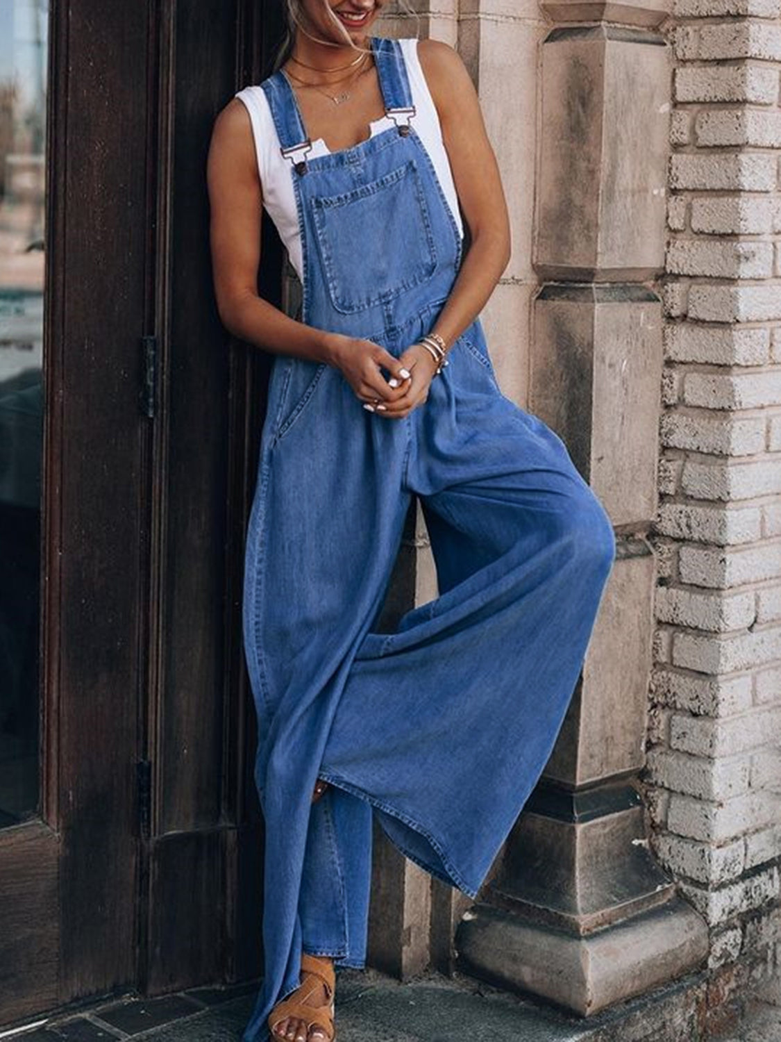 Woman wearing blue wide leg overalls posing against concrete wall