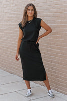 Woman wearing a black dress standing against a beige brick wall.