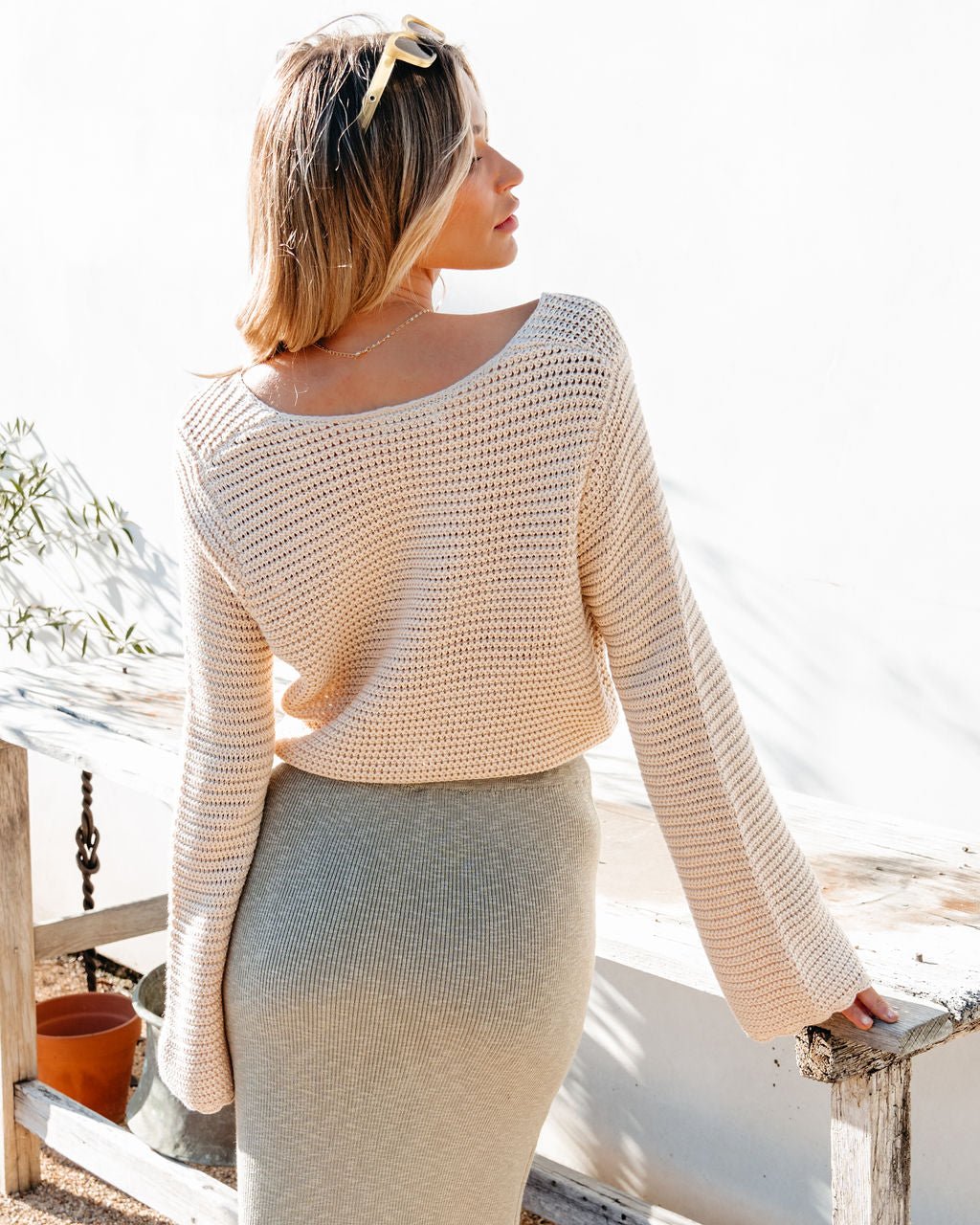Woman wearing a beige sweater top and light-colored skirt on a bright day.