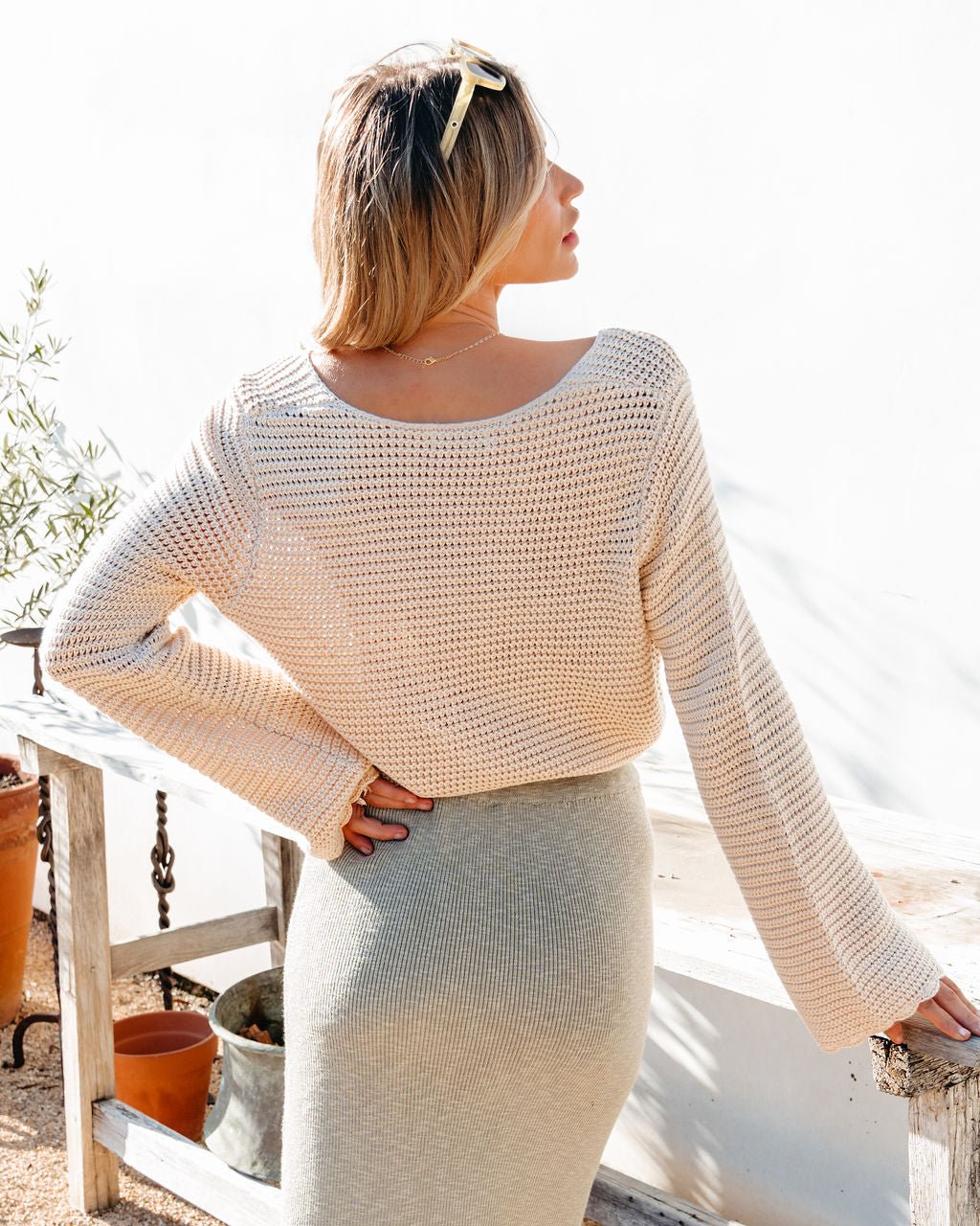 Woman wearing a beige knit sweater top and skirt standing outdoors.