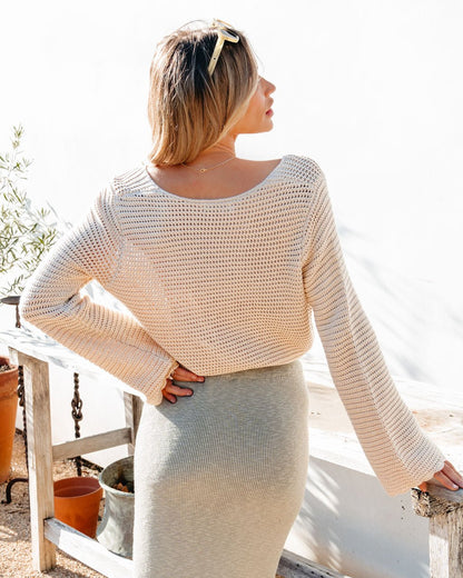 Woman wearing a beige knit sweater top and skirt standing outdoors.