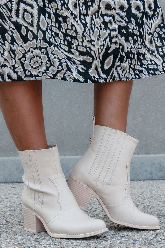 White ankle boots worn with a patterned skirt on a neutral background