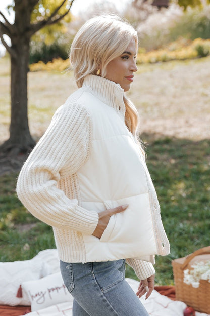 Woman wearing a cream-colored knit jacket outdoors with blurred background