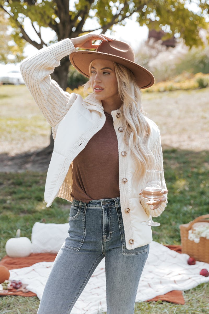 Woman in a cream cardigan jacket and brown hat enjoying a picnic outdoors.
