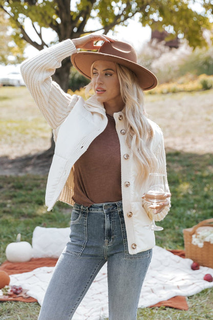 Woman in a cream cardigan jacket and brown hat enjoying a picnic outdoors.