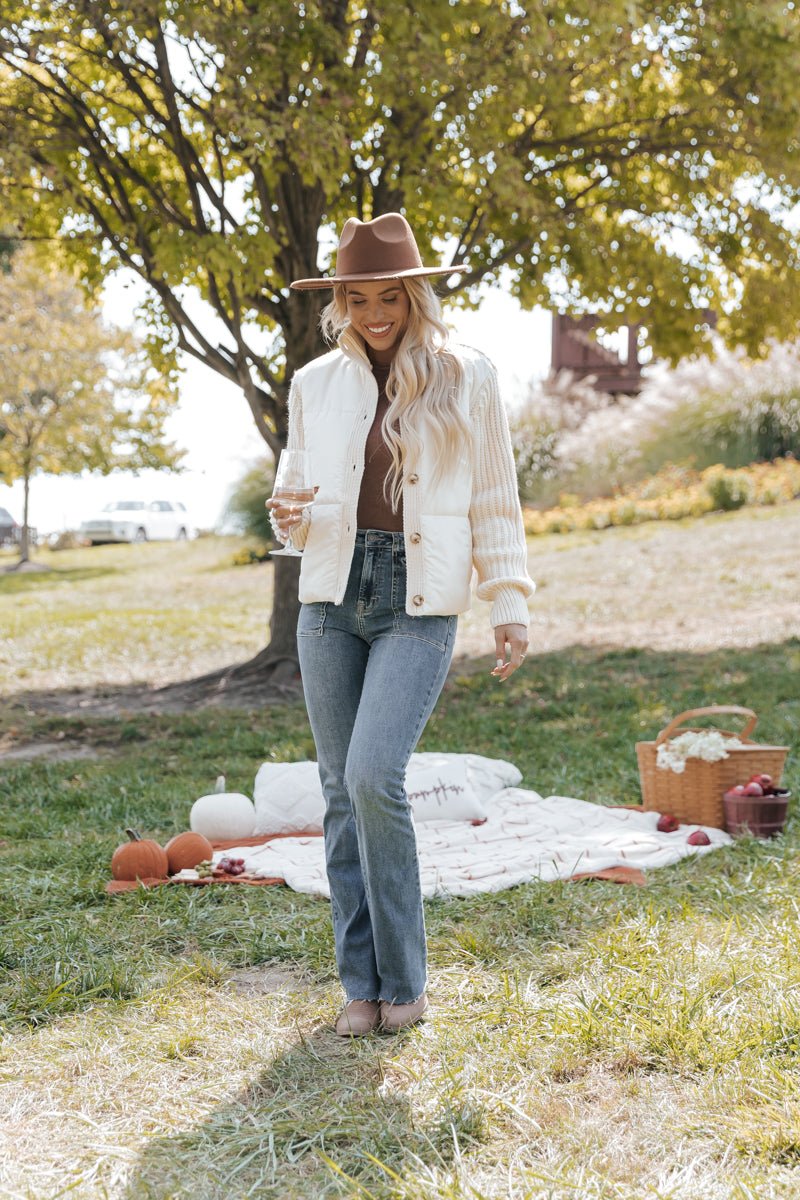 Woman in a cream jacket and hat standing in a park with a picnic setup.