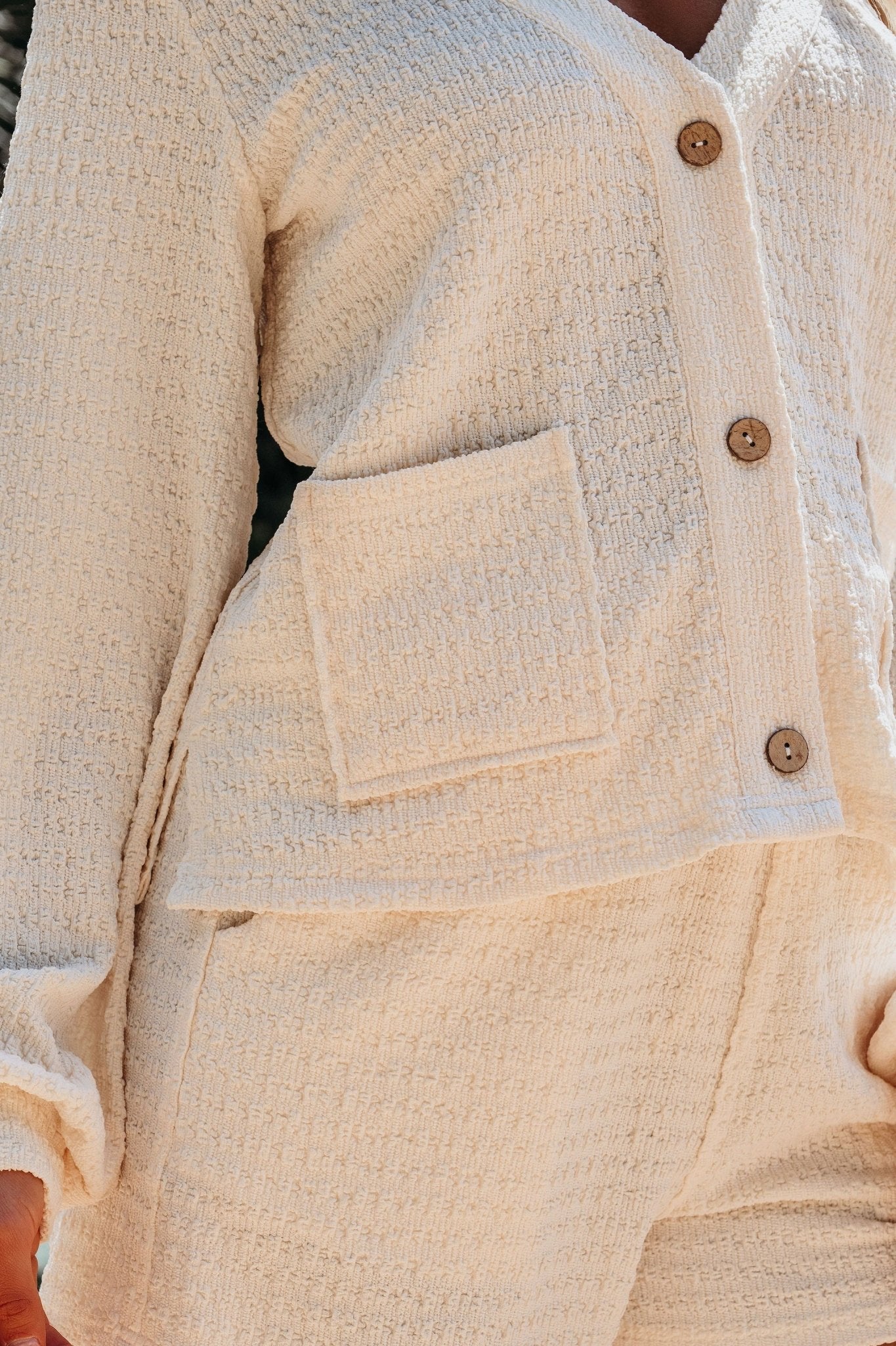 Close-up of a beige textured jacket and shorts set with buttons and a pocket.