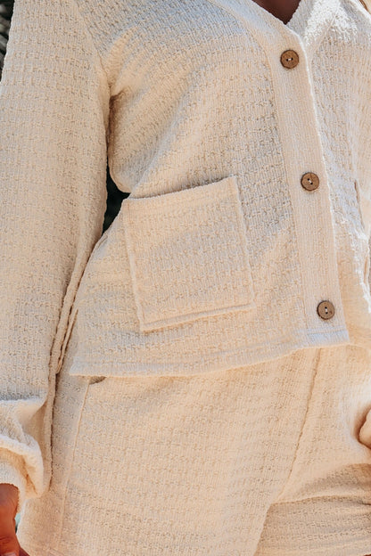 Close-up of a beige textured jacket and shorts set with buttons and a pocket.