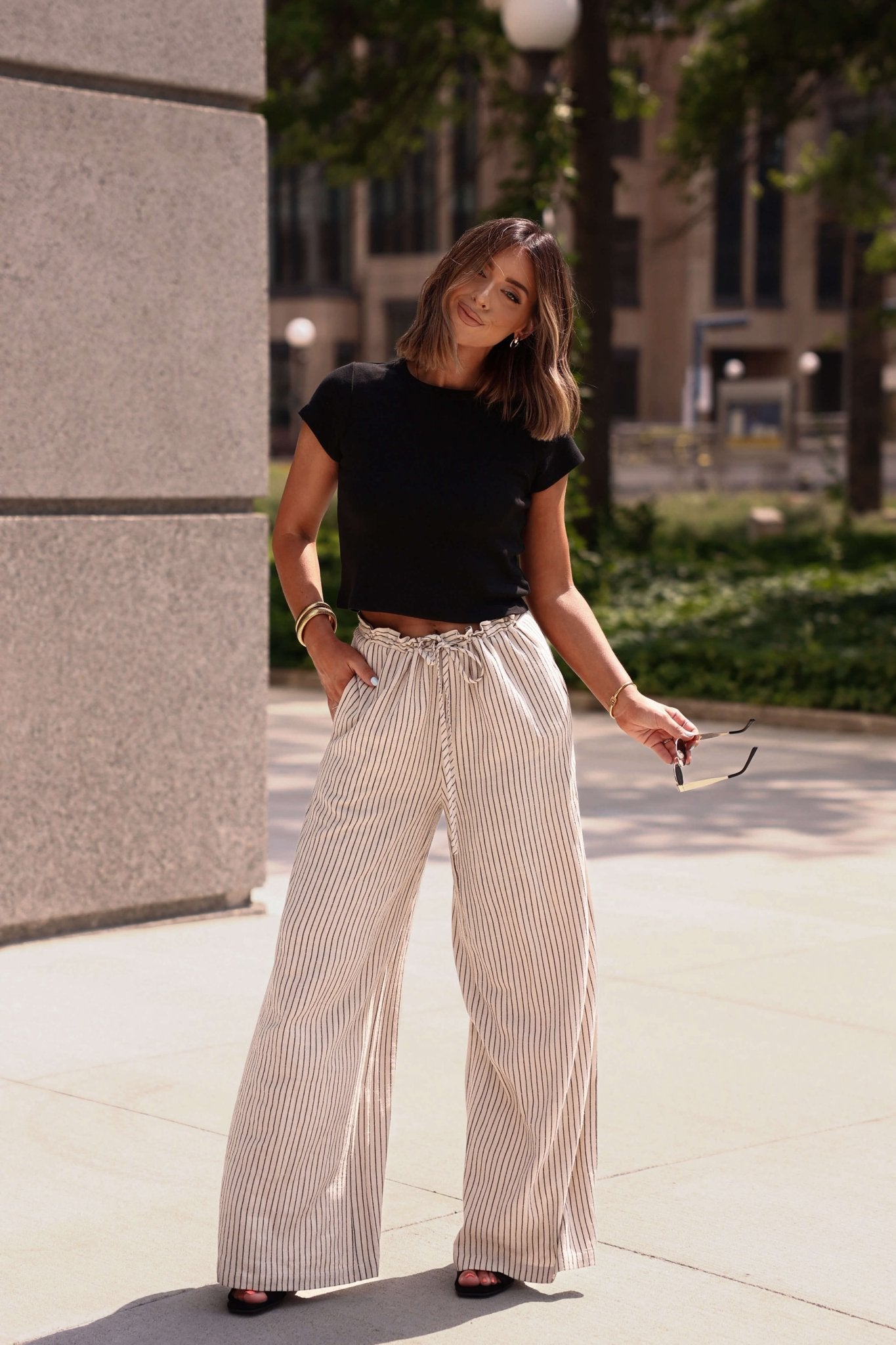 Woman wearing a black top and striped pants standing outdoors near a building.