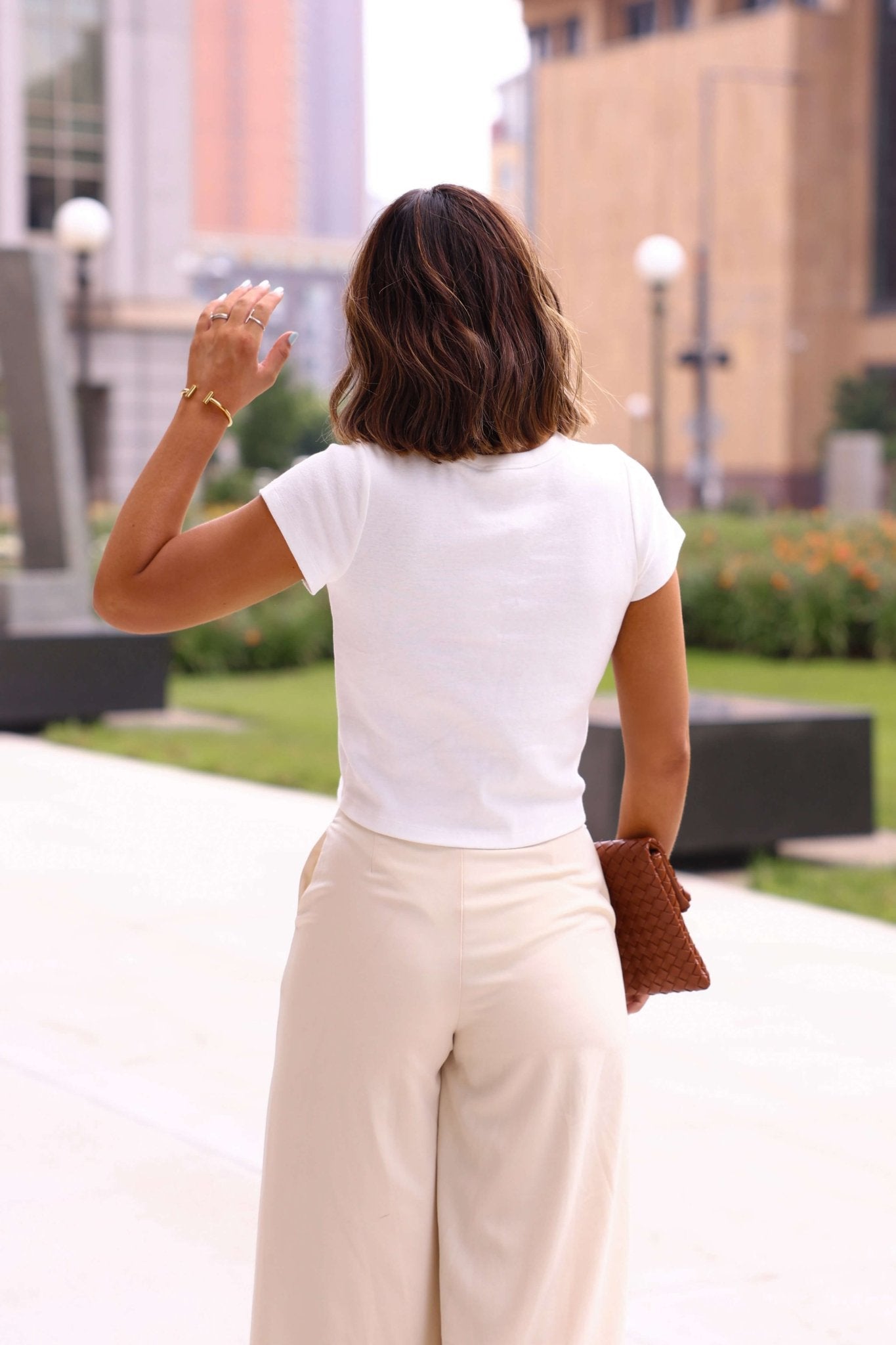 Woman in a white top and beige pants walking outdoors with a blurred background