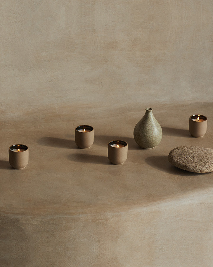 Set of ceramic vessels including a vase and multiple candle holders on a beige surface.