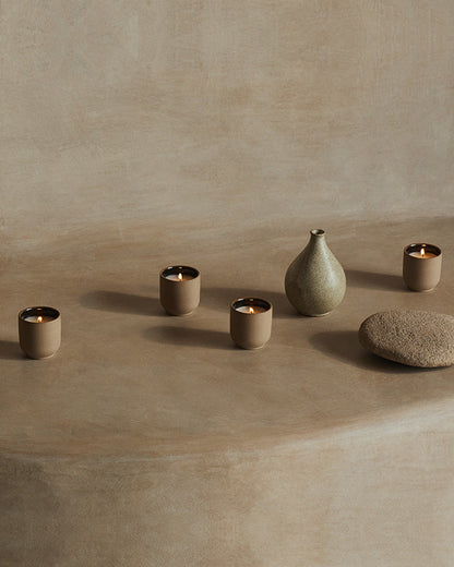 Set of ceramic vessels including a vase and multiple candle holders on a beige surface.