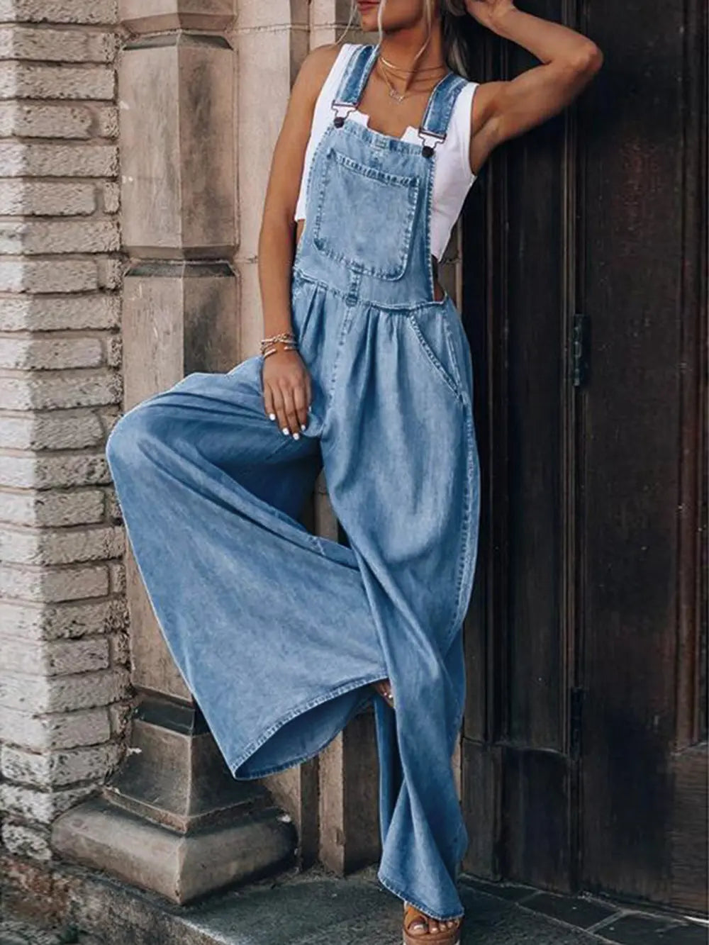 Woman wearing blue wide leg overalls posing against concrete wall